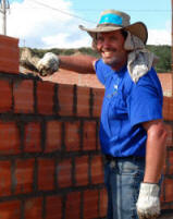 Smiling volunteer in a blue shirt and wide brimmed hat laying bricks