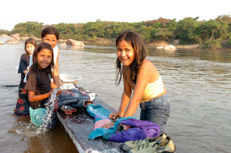 Four youngsters standing in river washing clothes and smiling