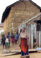 Woman in front of house with cracked mud walls