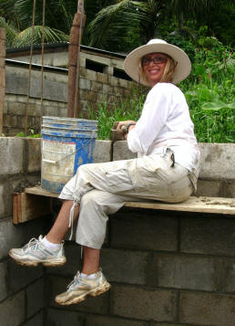 Volunteer sitting on scaffold working on concrete block wall